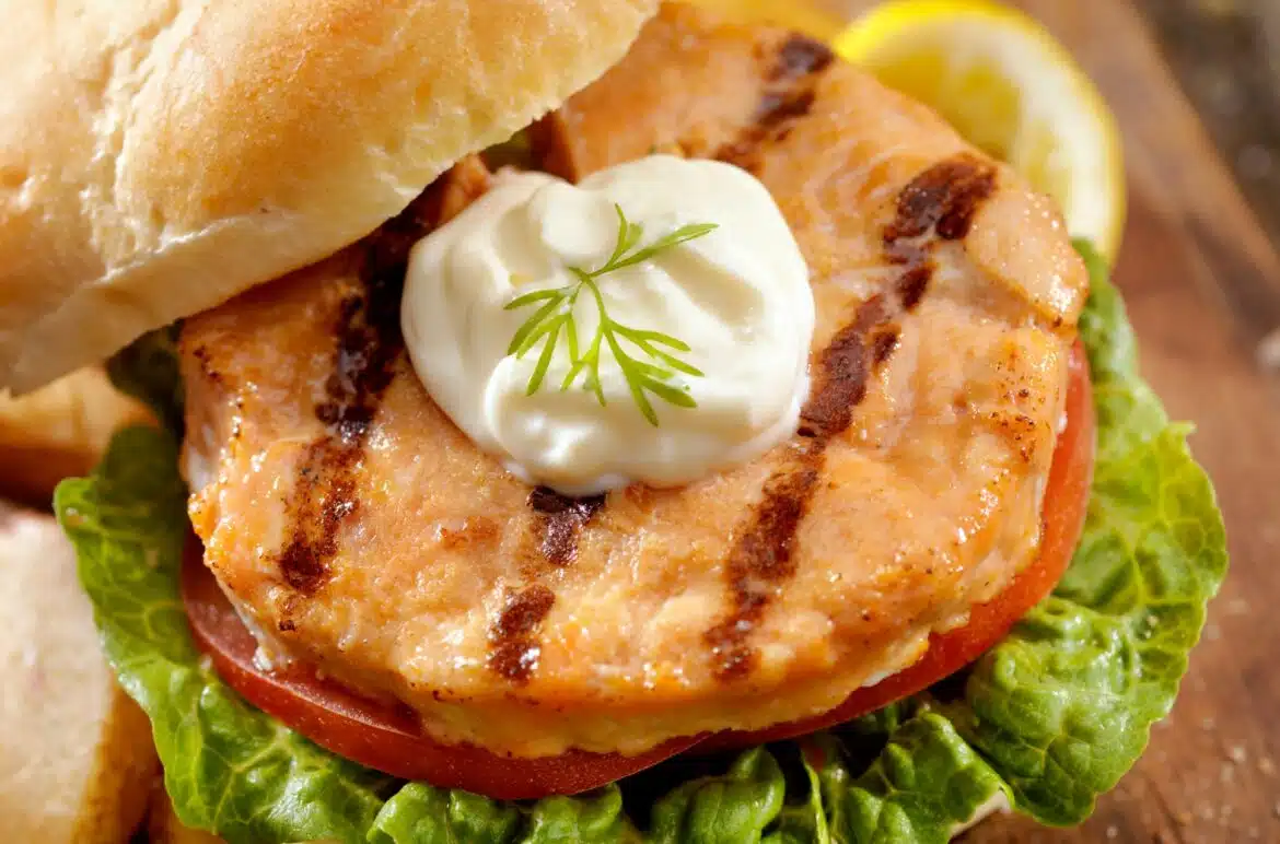 Lemon-Dill Salmon Burgers With A Dollop Of Dressing And Sliced Lemon Wedge
