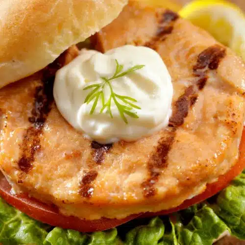 Lemon-Dill Salmon Burgers With A Dollop Of Dressing And Sliced Lemon Wedge